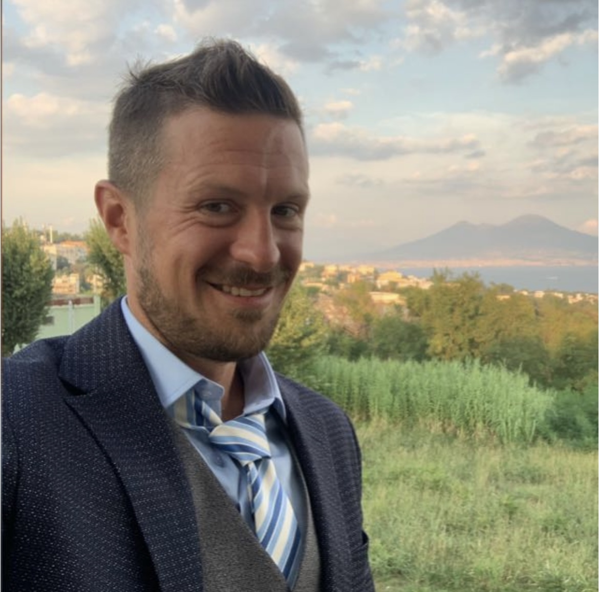 Uomo che sorride con un prato verde sullo sfondo.